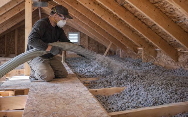 Installer topping up an Innisfil attic with blown-in cellulose insulation between the trusses