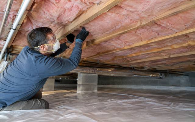 Installer insulating the floor joists over a crawl space with a vapour barrier on the ground in Innisfil